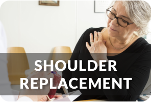 A doctor uses the model of a shoulder to show a patient the issue with her shoulder. The patient is holding her right shoulder with her left hand. Title reads; Shoulder Replacement